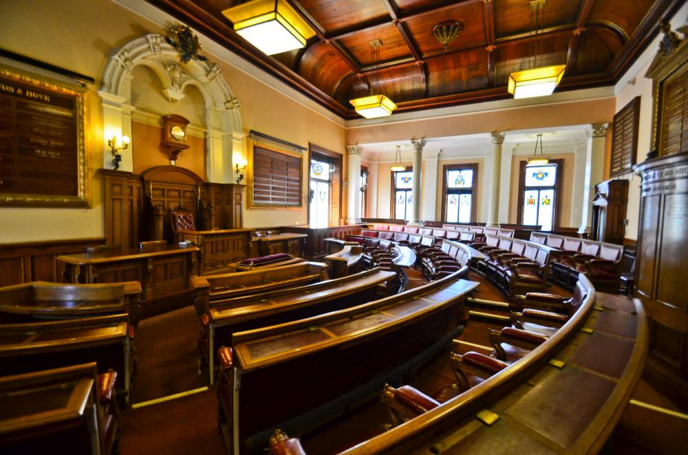 The Council Chamber. A very large room with curved booths of chairs.  Orange lighting and 5 stained glass windows