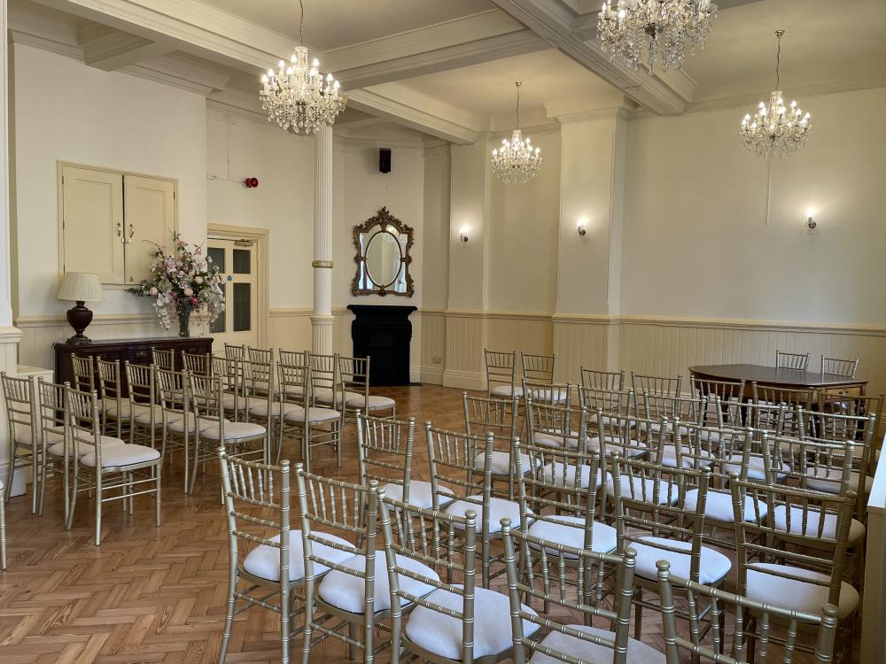 The Regency Room. Side view of chairs and aisle. Large mirror on the wall. Chandeliers on the ceiling.