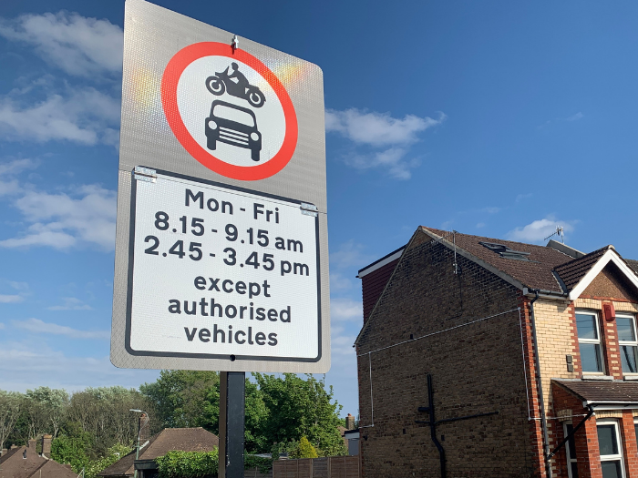 "A picture of a road sign with access restriction details with a house and blue sky"