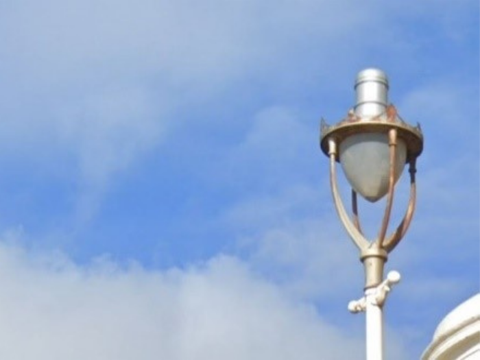 "A single streetlight at the top of a lamppost with four metal strips surround it"