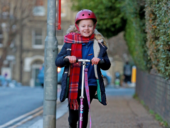 "girl in a school uniform on a scooter, scooting on a pavement"