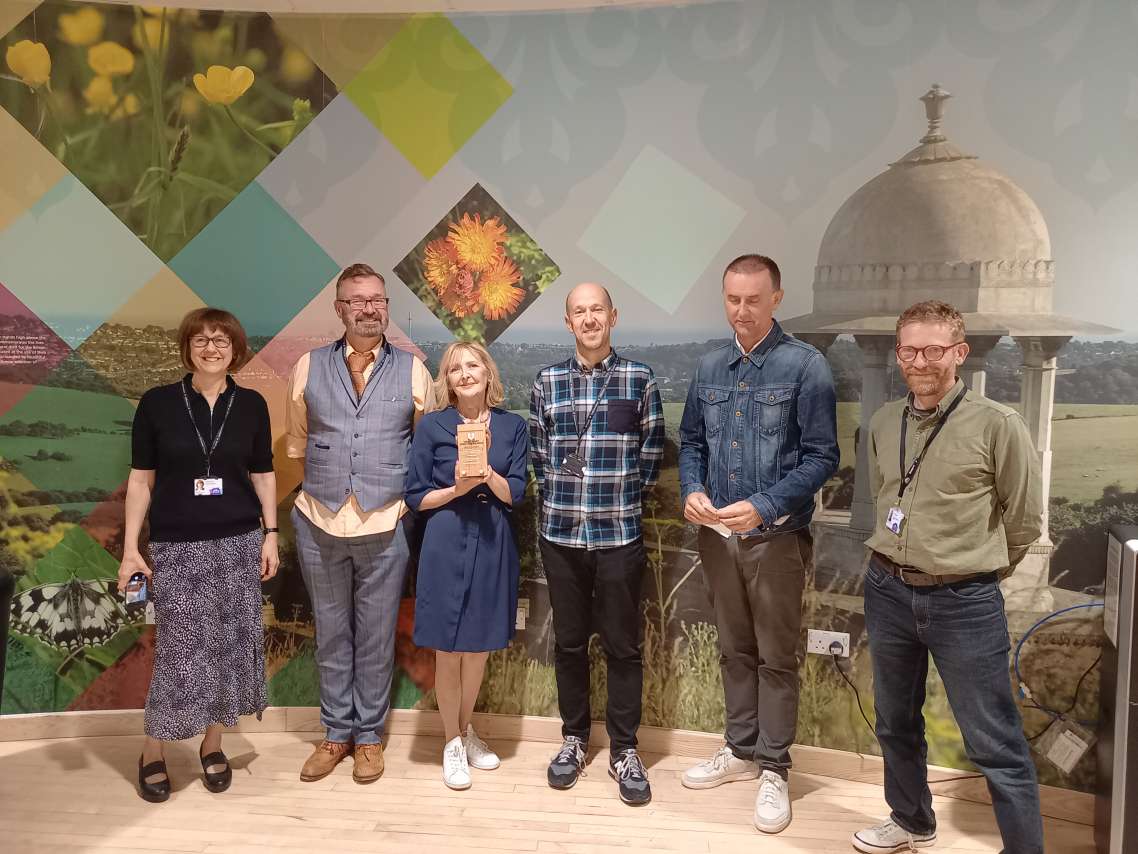 Five members of the project team with councillor Gill Williams holding the award against a background of a mural showing scenes from Brighton & Hove