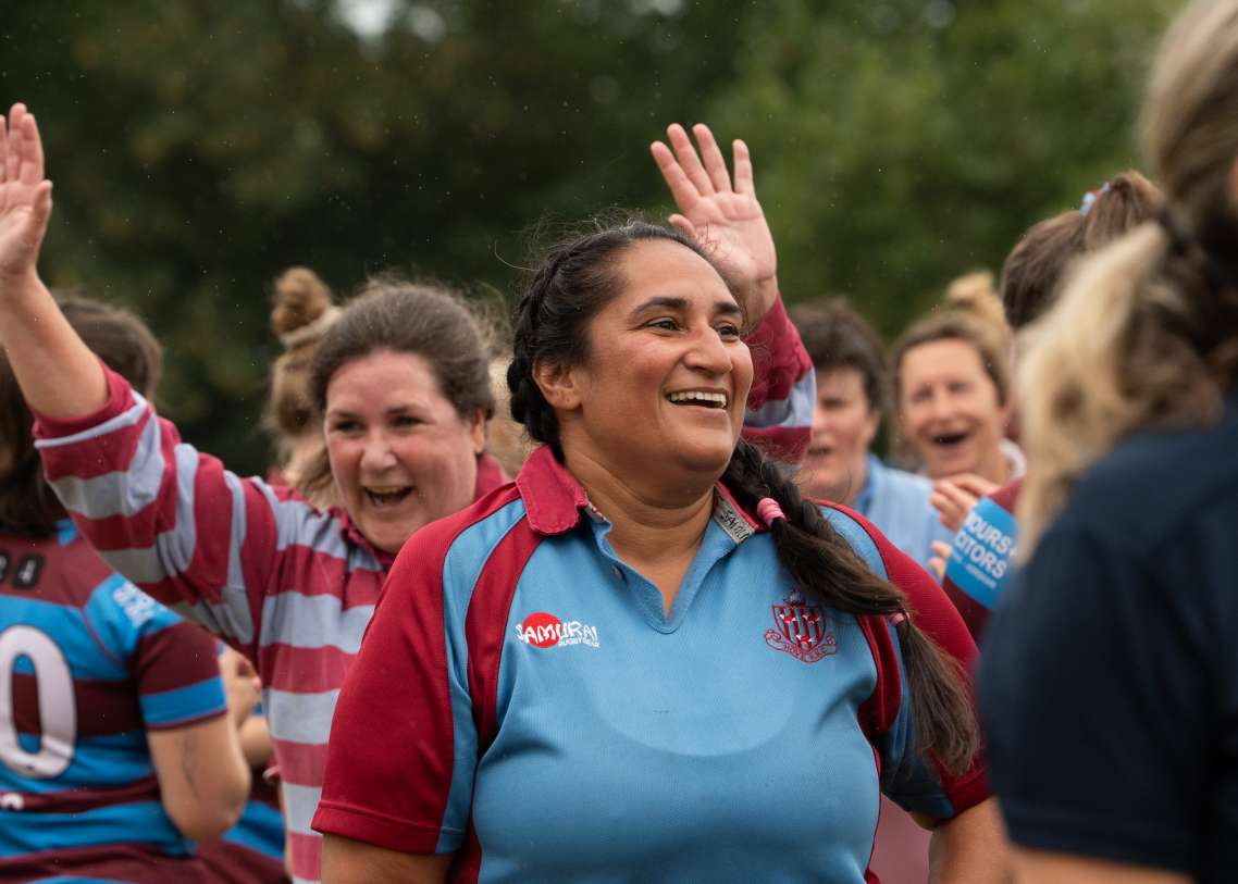 A women in a blue rugby shirt is smiling while other women stand behind her and cheer