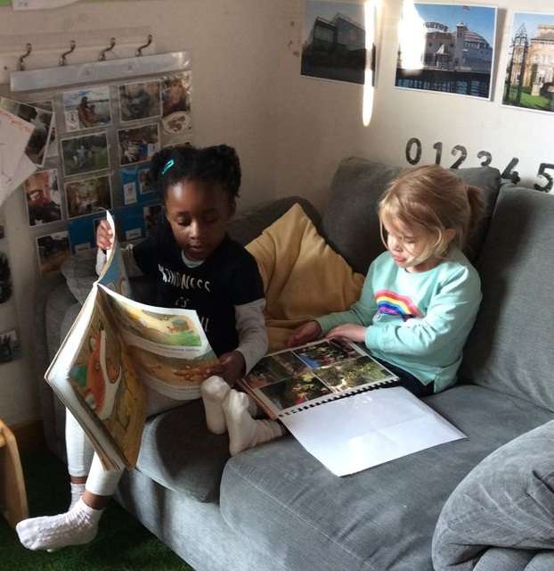 "two young children sitting on a sofa looking at books"