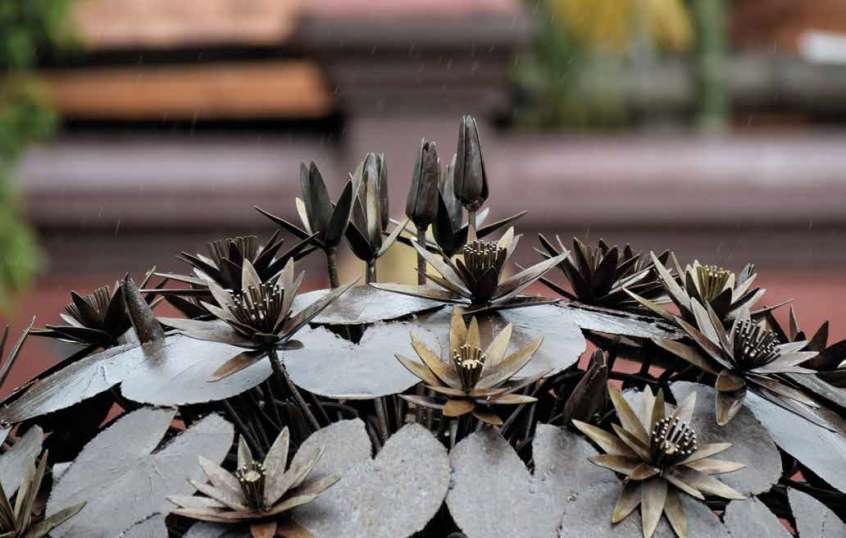 Spherical metal structure made of lily pads on stalks with metal flowers emerging between them