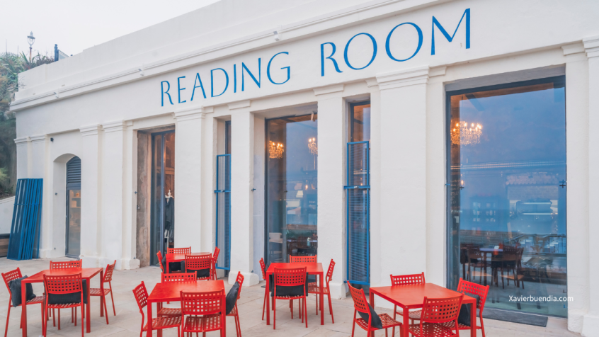 Photograph of the newly restored Reading Room. There are red tables and chairs on the terrace outside the large floor to ceiling windows.