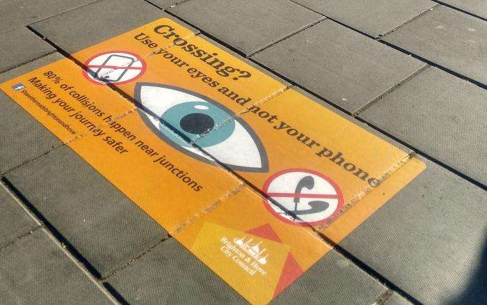 Poster painted on the pavement to warn people "use your eyes and not your phone" when crossing a road.
