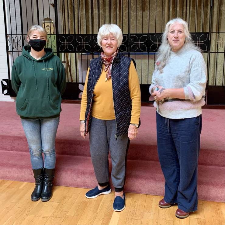 Three volunteers stand in front of the gates at St Richard's Community Centre.