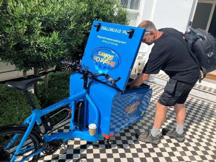 Bruce reaches into the open compartment on the front of his blue eBike. He's parked outside of a customer's home.