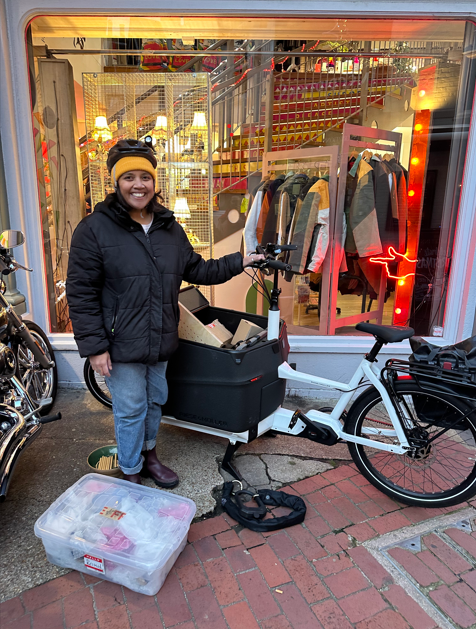 Person smiling standing in front of a shop holding onto the handle bars of an eCargo bike.