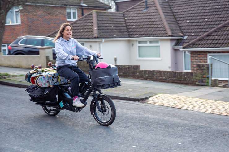 Sarah riding her ecargo bike with muliple colourful skateboard strapped to the back