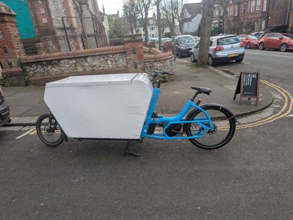 a blue eCargo bike is parked on a street corner in Brighton