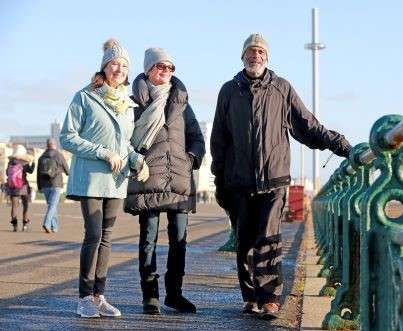 Three people standing on Brighton seafront, smiling at the camera.