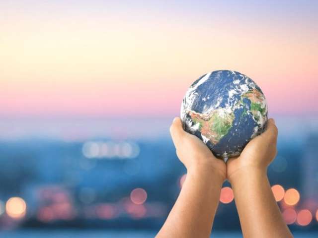 Child holding up a model of the planet against a sunset sky.