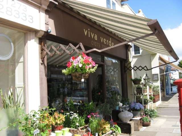 Exterior of local shop in a parade with stripy awning and hanging baskets outside