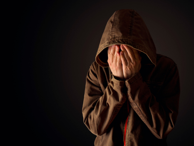 Distressed person covering their face with their hands.