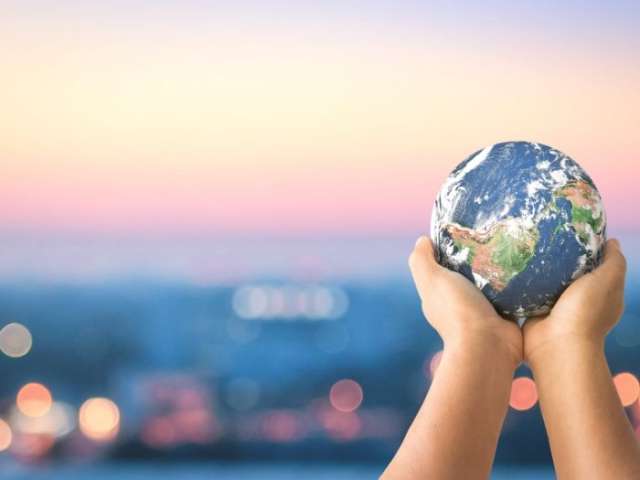 Child's hands holding a globe of the world with a city at sunset in the background 
