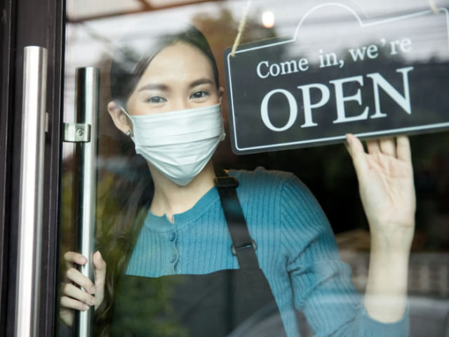 Woman shopkeeper at the door of the premises turning the sign to 'Come in, we're open'.