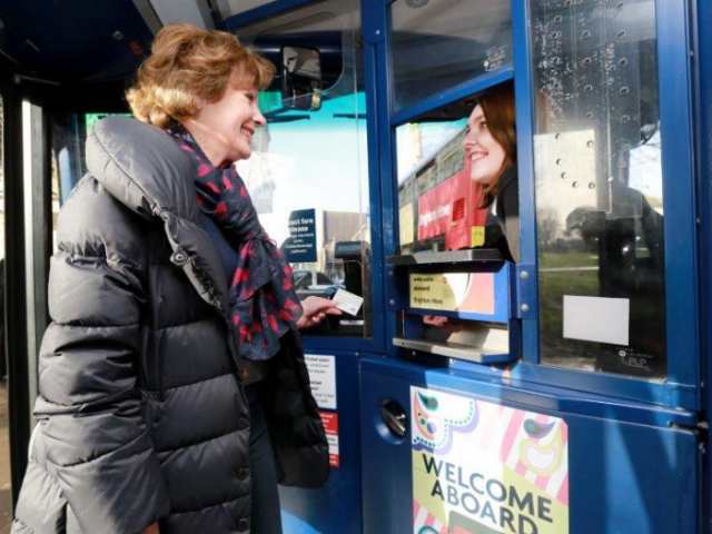 Lady getting on a bus and smiling with the driver
