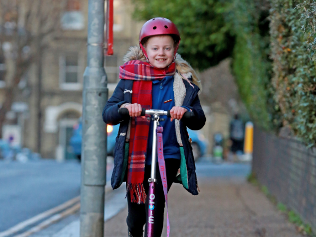 A schoolgirl on a scooter, scooting along a pavement