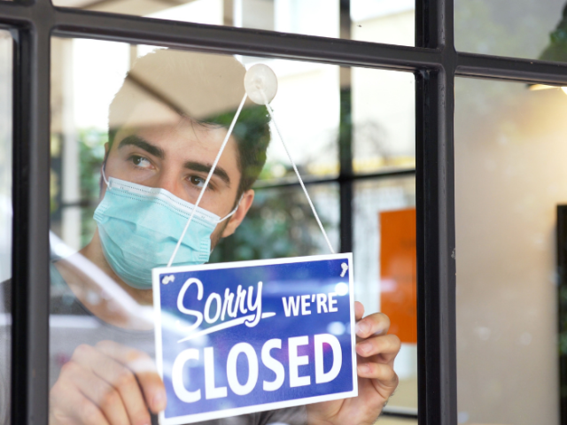 Working wearing a mask in a business with a 'Sorry we're closed' sign in the window