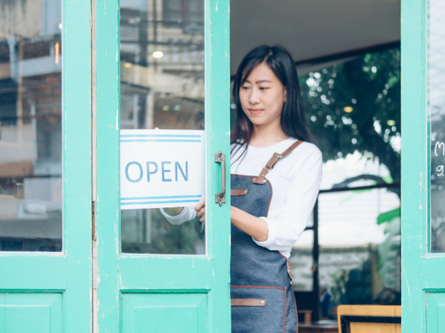 A small business owner putting up an 'Open' sign in a shop front