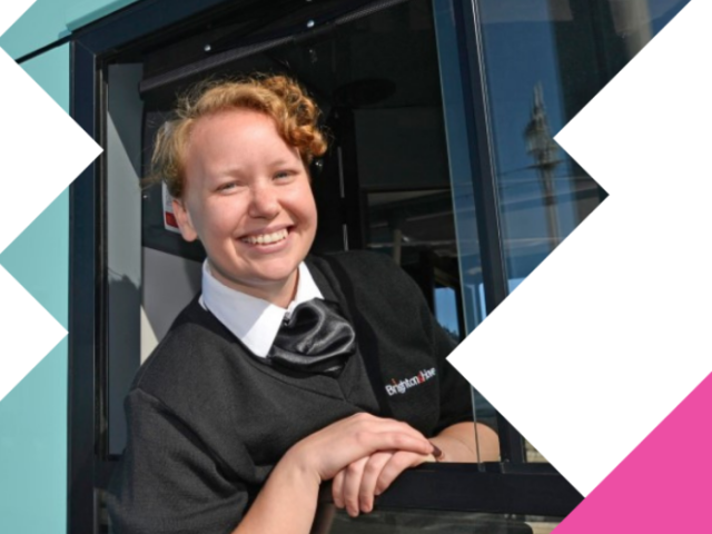 A woman sitting in the drivers' seat of a bus smiling out of the window