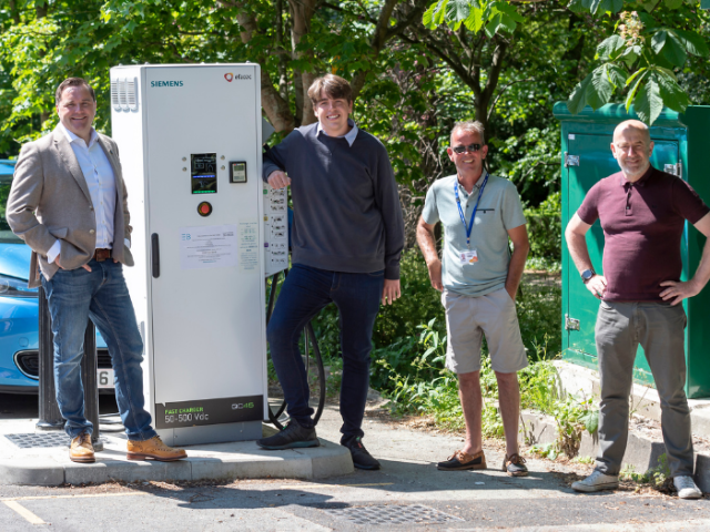 A picture of four men standing next to an electric vehicle charging hub