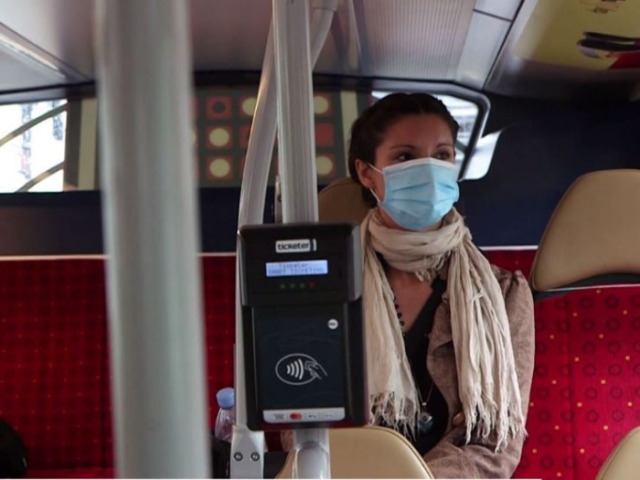 A woman sitting on a bus wearing a face mask