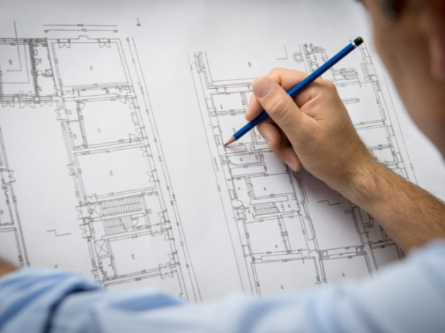 Hand holding a pencil, putting finishing touches to a floorplan for a building.