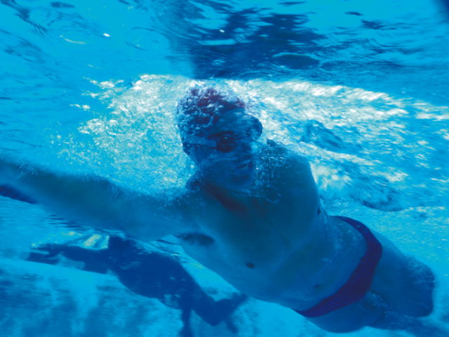 A swimmer with a swimming cap and goggles on flying through the water at an indoor swimming pool with the picture taken from underneath 