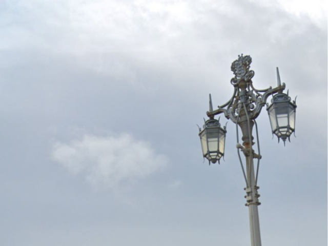 A streetlight with 2 glass lanterns hanging from a patterned bracket.