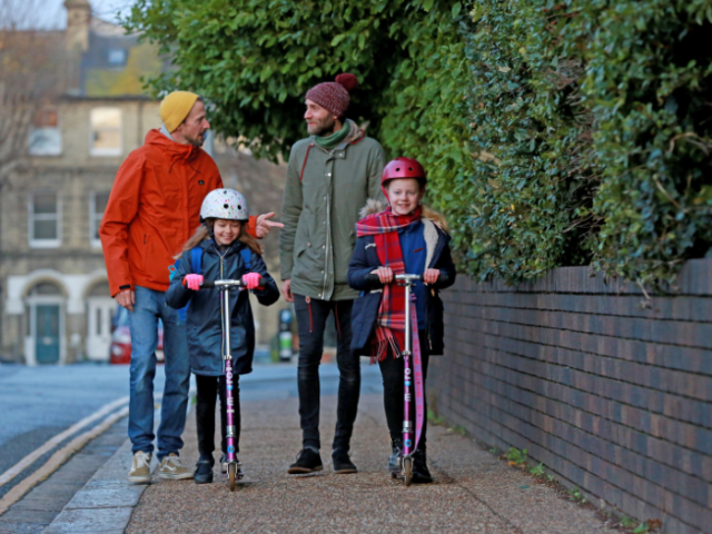 Two girls on scooters in front of two men