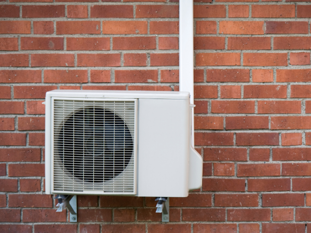 Photograph showing a heat pump attached to the wall of a house