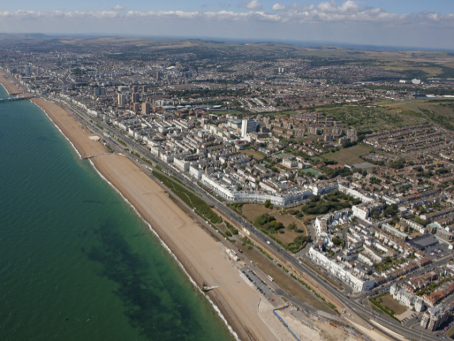 An aerial view of the city of Brighton & Hove showing the sea, the beach and the city stretching out towards to South Downs.