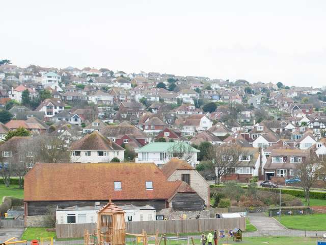 A view of Saltdean taken from Saltdean Oval Park showing the playground in the foreground with houses rising up the hill filling the horizon to the sea. 