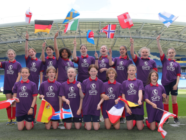 Picture of young football players at the Brighton & Hove Community Stadium waving flags from the countries competing in UEFA Women's EURO 2022