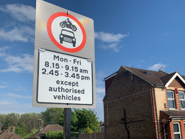 A picture of a road sign with access restriction details with a house and blue sky