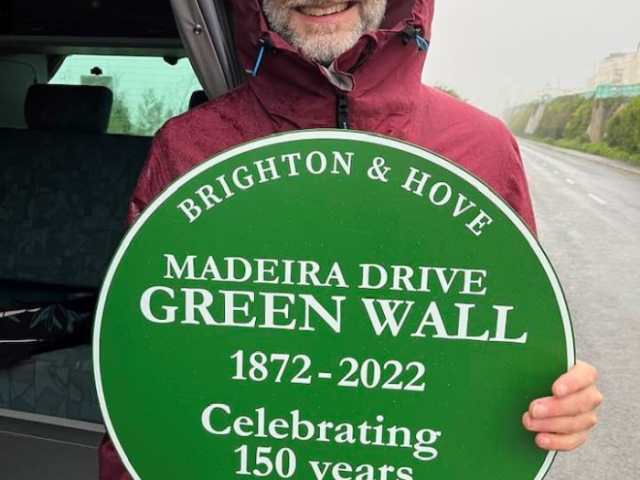 Person holding a green plaque commemorating 150 years of the Green Wall