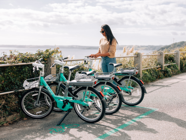 Three bikes parked on a pavement with a woman looking at them