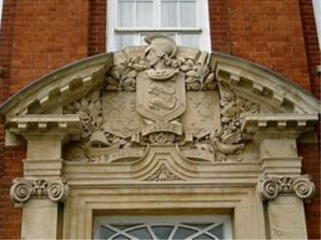 An ornate door white door surround with columns either side supporting a semi-circular top feature, the centre of which is a shield and bust.orting an  