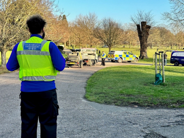 Photograph of an environmental enforcement officer watching Sussex Police check vehicles for insecure loads.