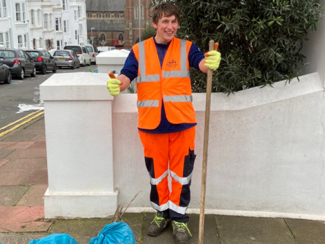 Photograph of young man smiling at the camera with a sweeping brush.