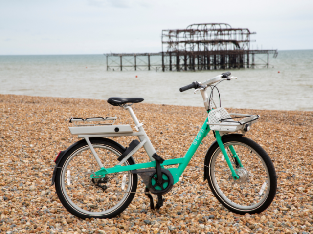 A green bike on a beach with a pier in the background