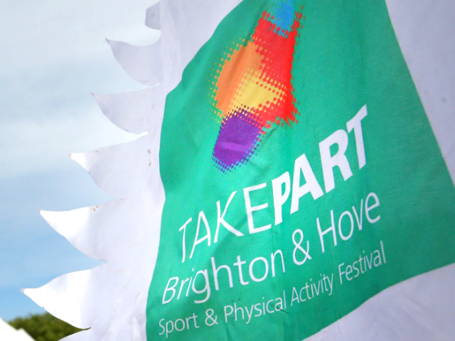 Photo of a flag flying outside with the TAKEPART logo on it