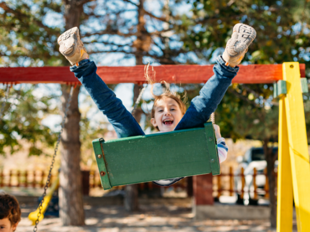 Photograph of a child wearing jeans swinging high in the air and smiling at the camera.