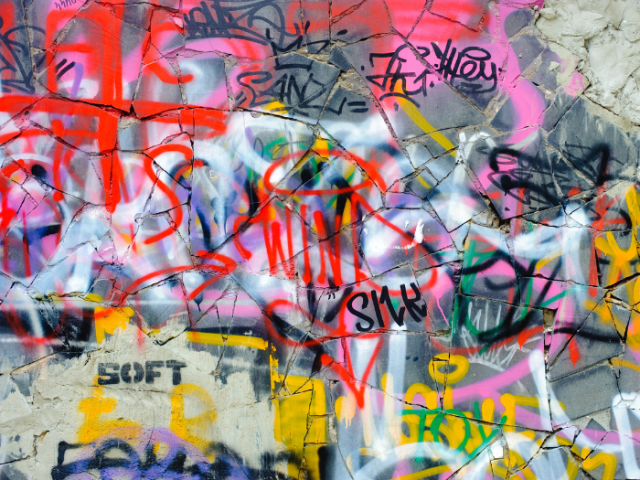 Photograph of graffiti tags in red, pink and yellow spray paint.