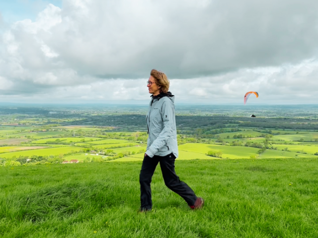 A person walking in the countryside with a paraglider in the background