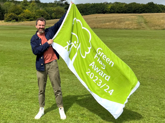 Photograph of a man holding a large green flag that reads 'Green Flag Award 2023/24'.