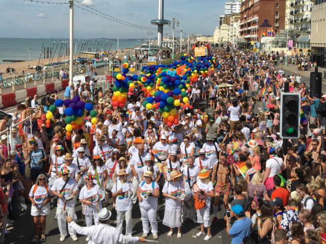 A photo of a group of people carrying rainbow coloured balloons in the Pride Community Parade on Brighton & Hove seafront